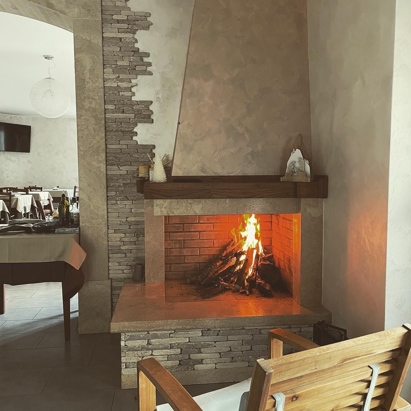 Accogliente soggiorno con camino acceso, rivestimento in pietra e sedia in legno in primo piano.