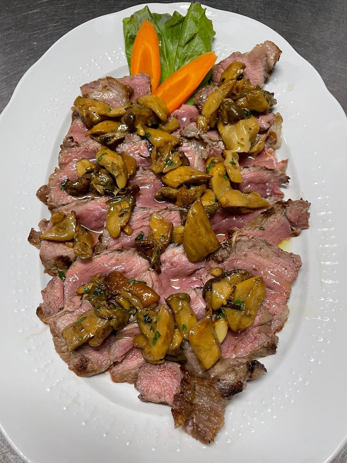 Fettine di bistecca impiattate, guarnite con funghi e servite con contorno di carote e lattuga.
