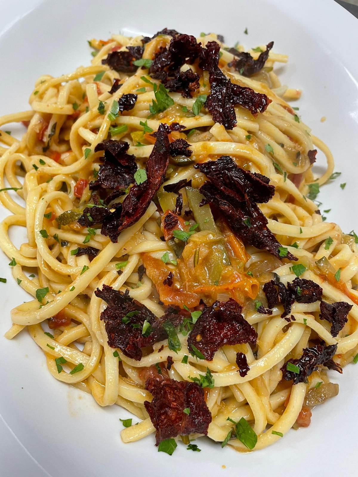 Spaghetti alle erbe aromatiche e pomodori secchi su un piatto bianco.