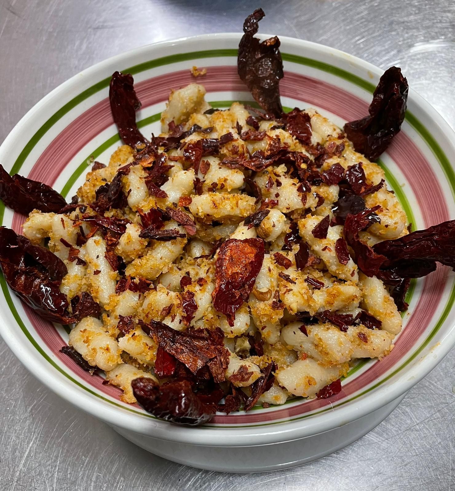 Una ciotola di pasta condita con salsa rosso scuro e pezzetti di formaggio su un piano di lavoro in metallo.