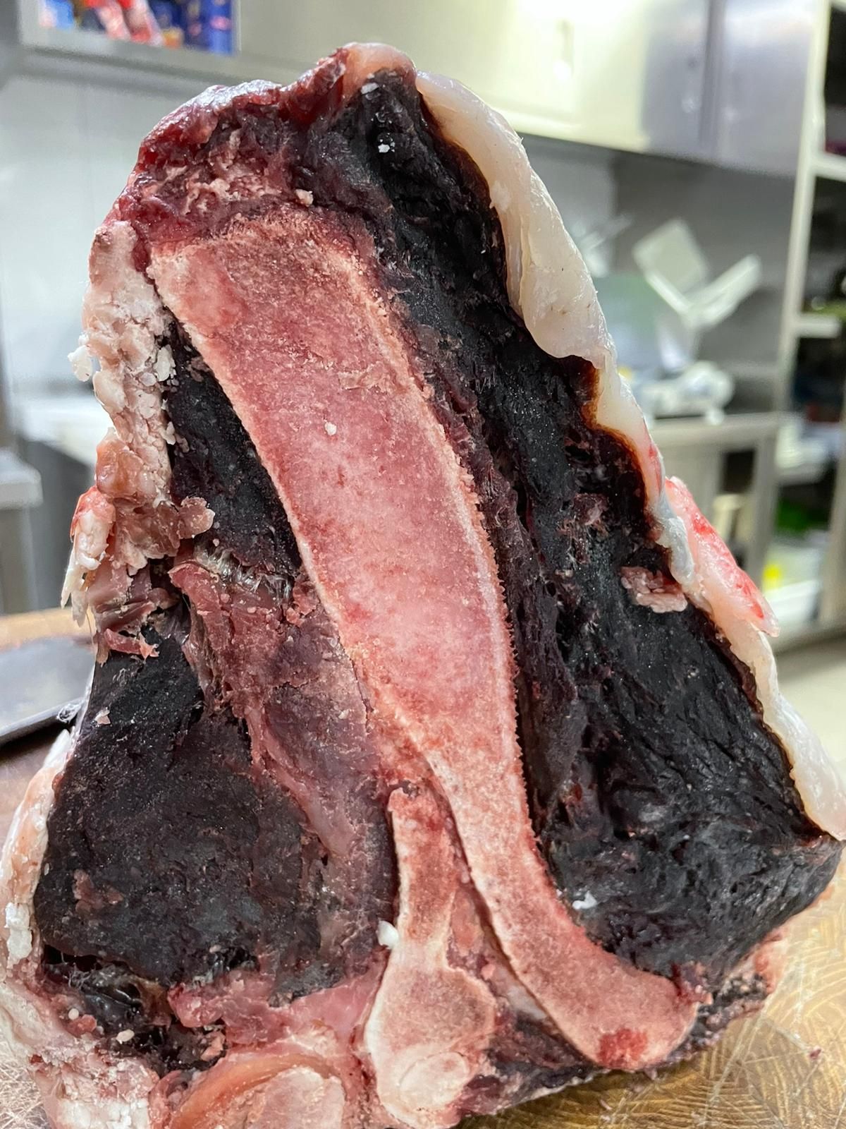 Sezione trasversale di carne cruda con crosta esterna scura e centro rosa su una superficie di taglio