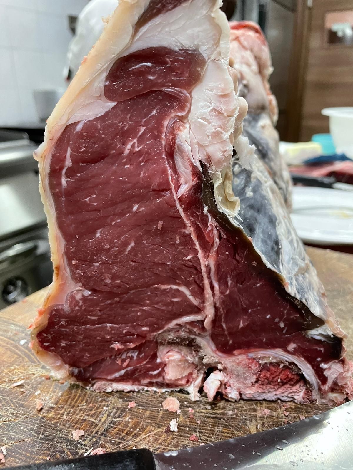 Primo piano di un taglio di manzo crudo su un tagliere, che mostra la carne di un rosso intenso e il grasso in eccesso.