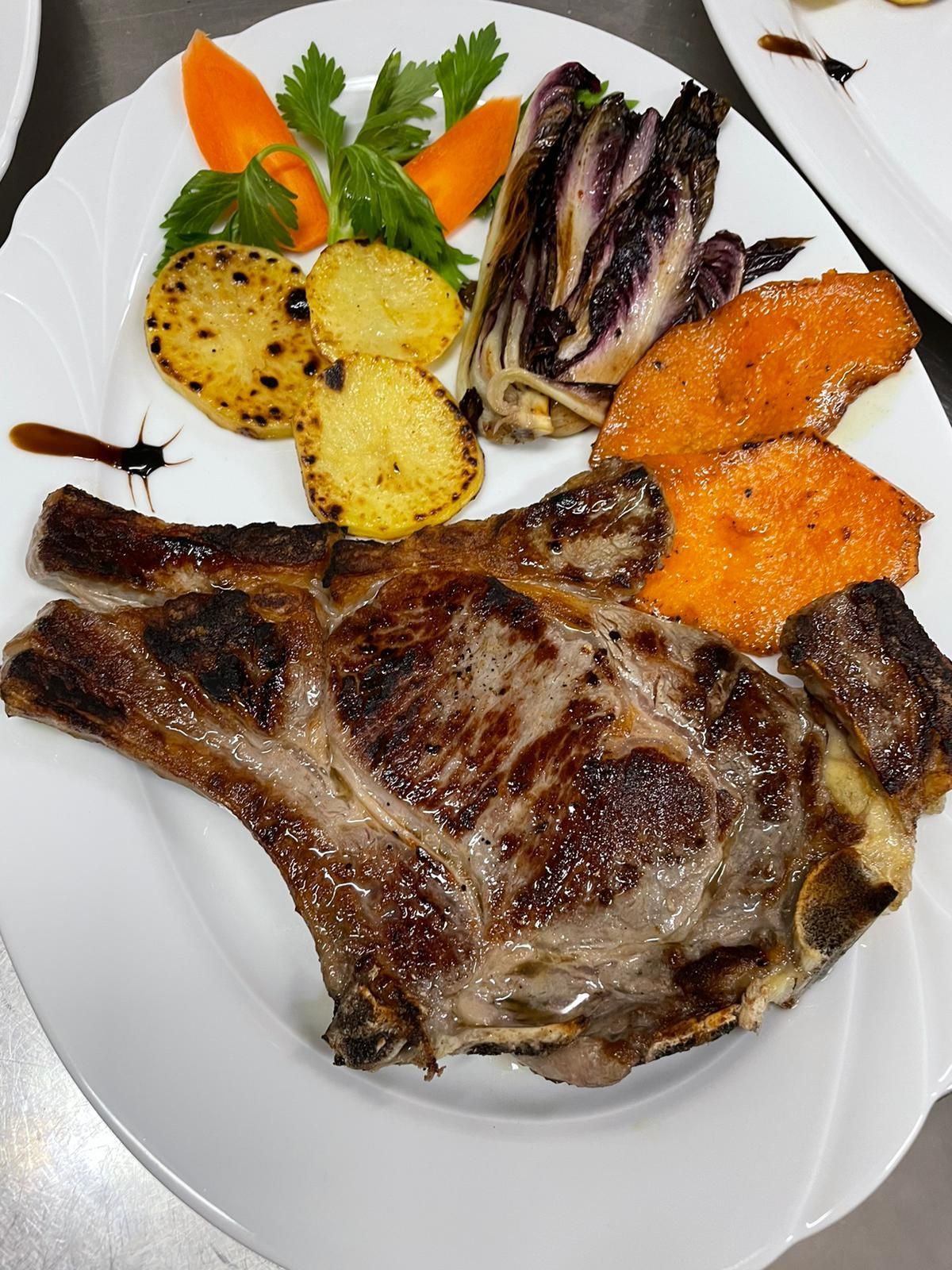Bistecca alla griglia con verdure arrosto e prezzemolo su un piatto bianco.