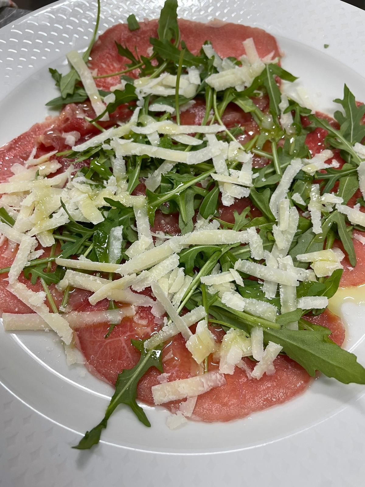 Salumi stagionati serviti su un piatto bianco, guarniti con rucola e scaglie di formaggio.