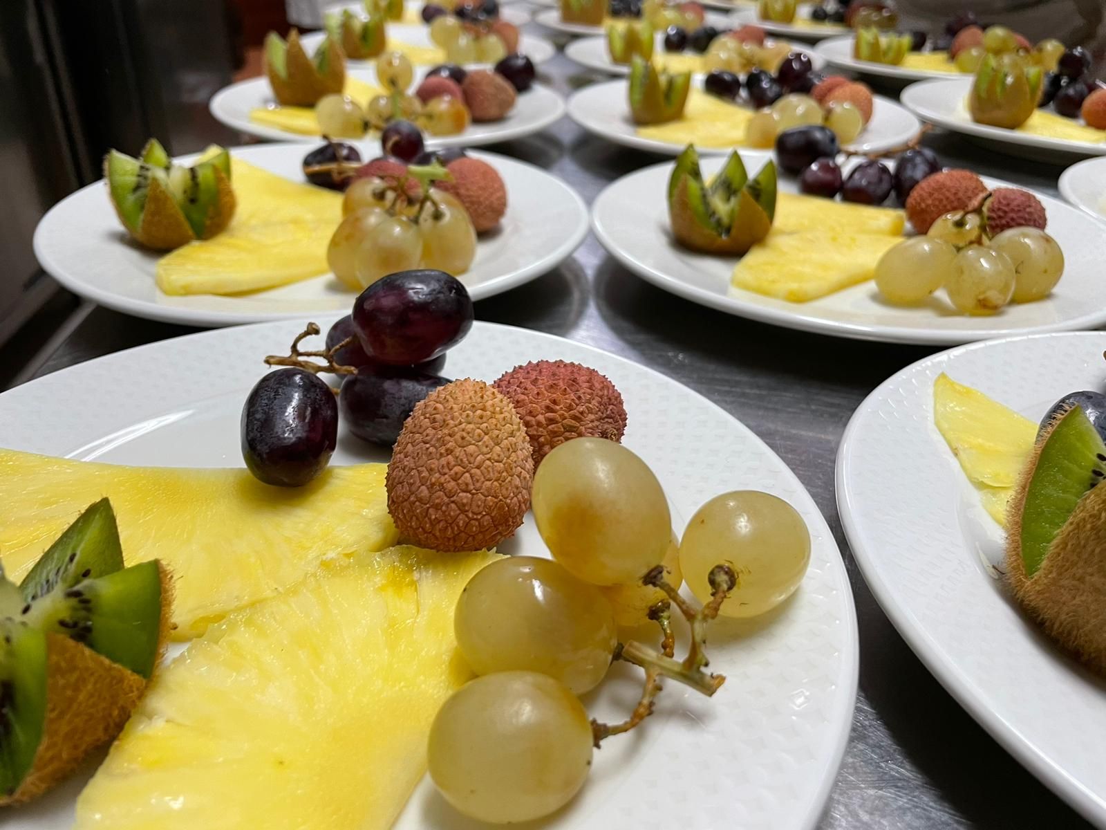 Su un tavolo, piatti con dessert di frutta assortiti, guarniti con uva, kiwi e litchi.