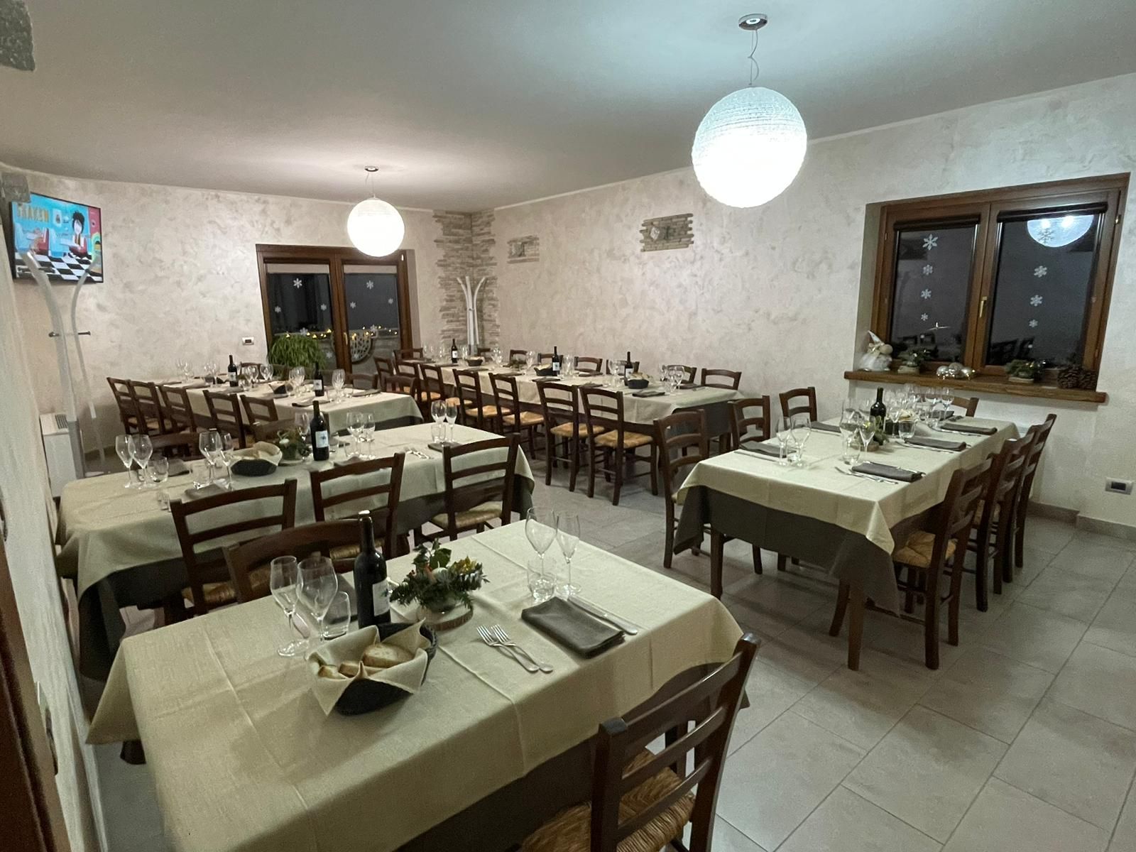 Sala da pranzo vuota di un ristorante, con tavoli apparecchiati con cura, sedie di legno e lampade a sospensione a forma di globo.