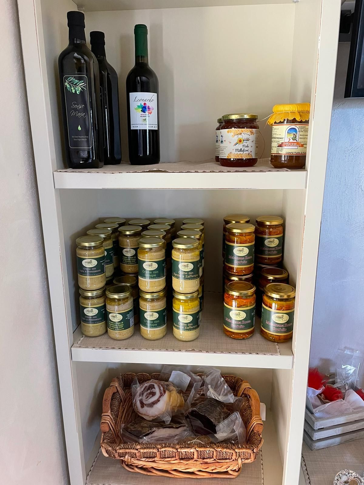 Scaffale della dispensa con bottiglie, barattoli, scatolette impilate e un cesto di cipolle e patate.