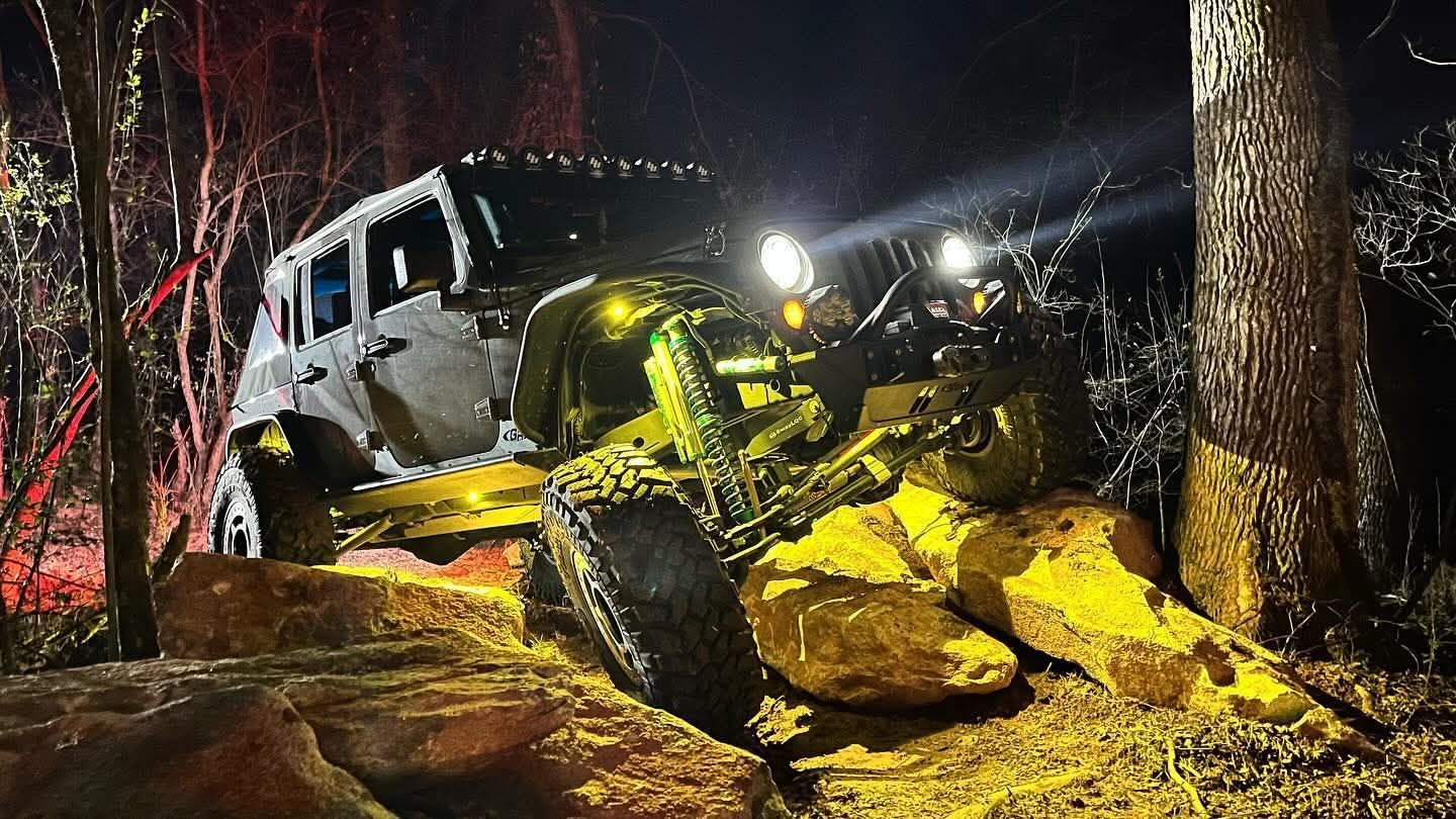 Off-road Jeep with bright headlights crawling over muddy rocks in a dark forest at night