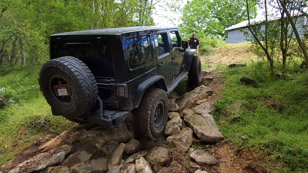 A black jeep is driving down a rocky path in the woods.