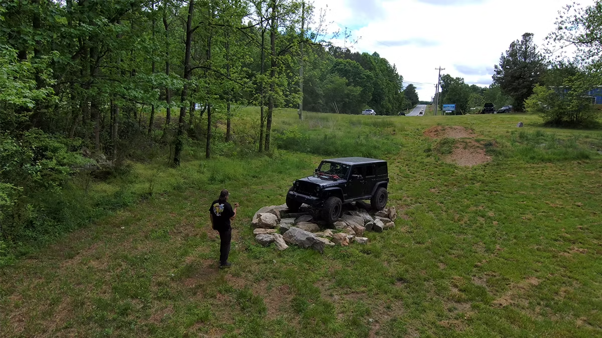 An aerial view of a man standing next to a jeep in a grassy field.