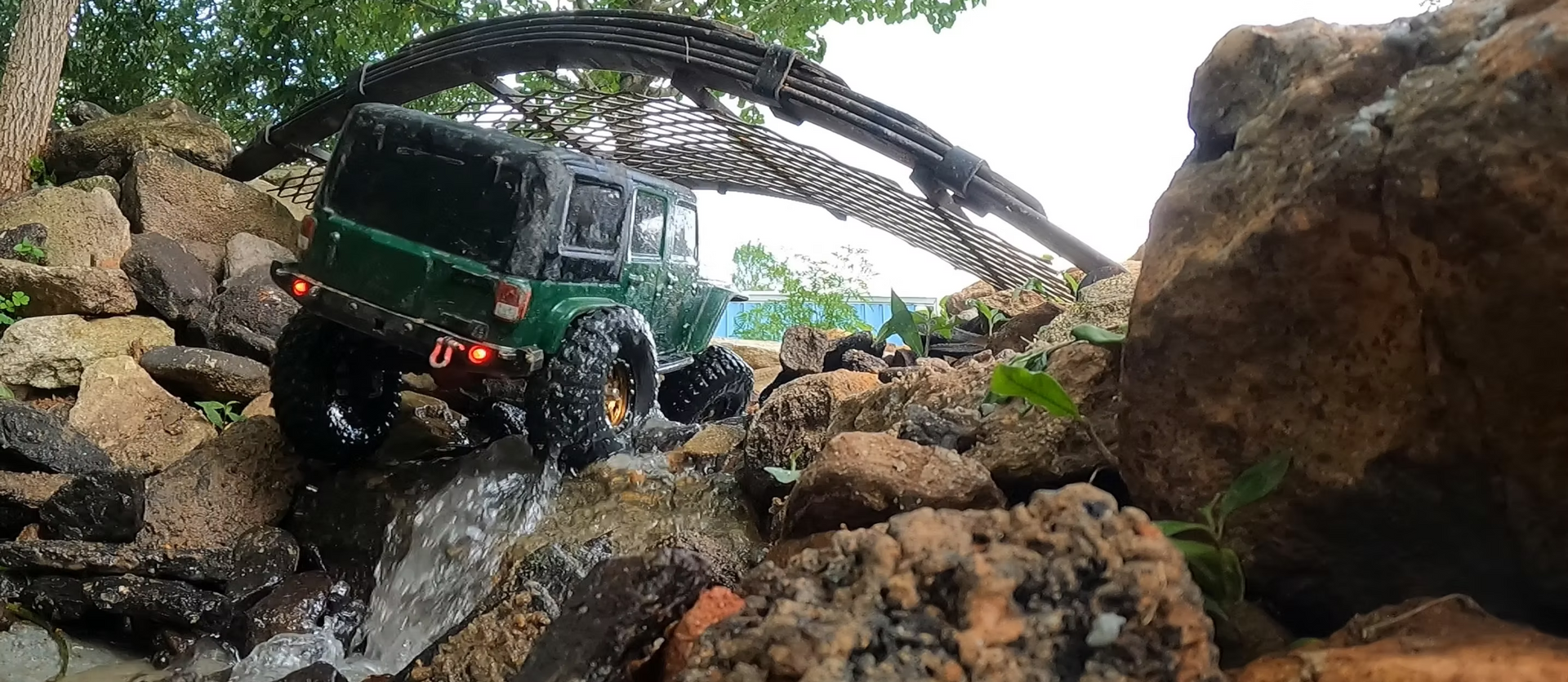 Green toy jeep climbing rocks, near a wooden structure.