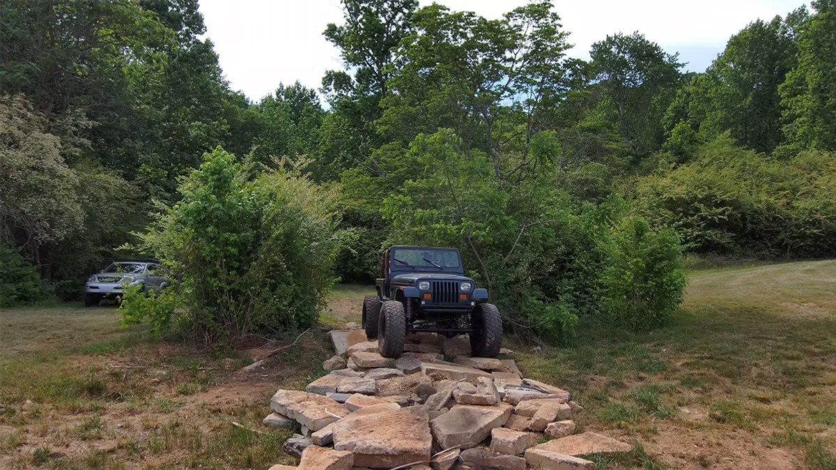A jeep is driving down a rocky path in the woods.
