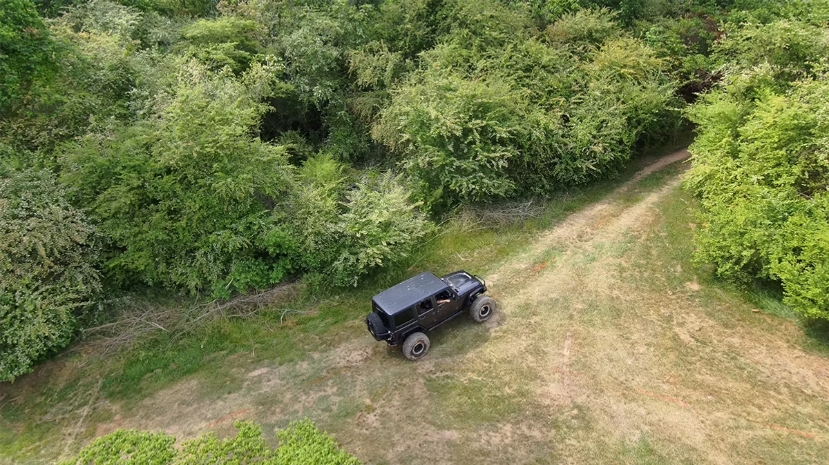 An aerial view of a jeep driving down a dirt road in the woods.