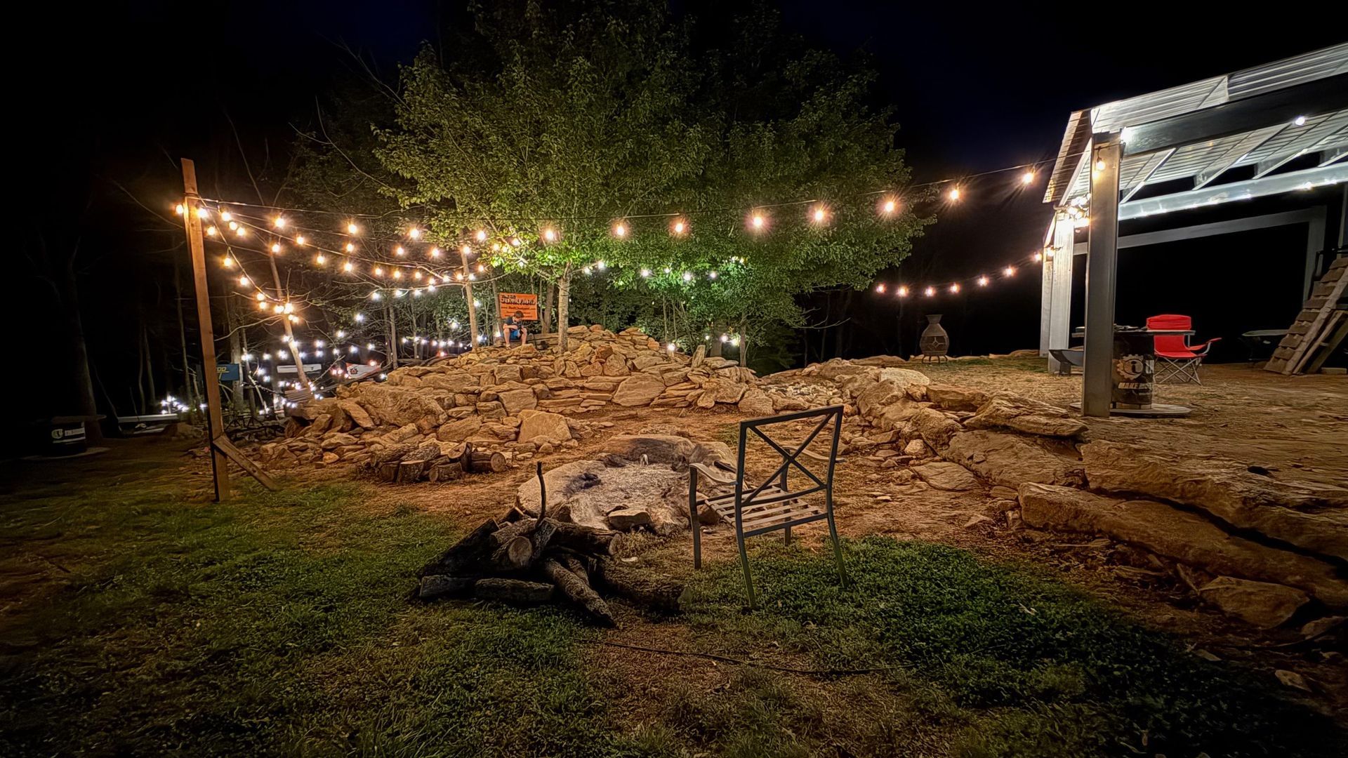 String lights over a rocky outdoor area at night beside a lit structure