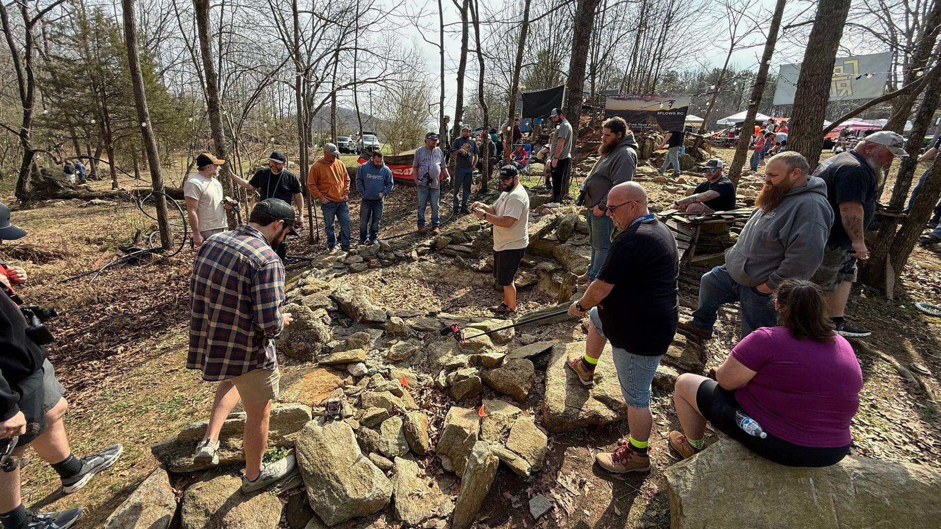 People gathered outdoors on rocky ground in a wooded area, working together in a cleanup or trail project.