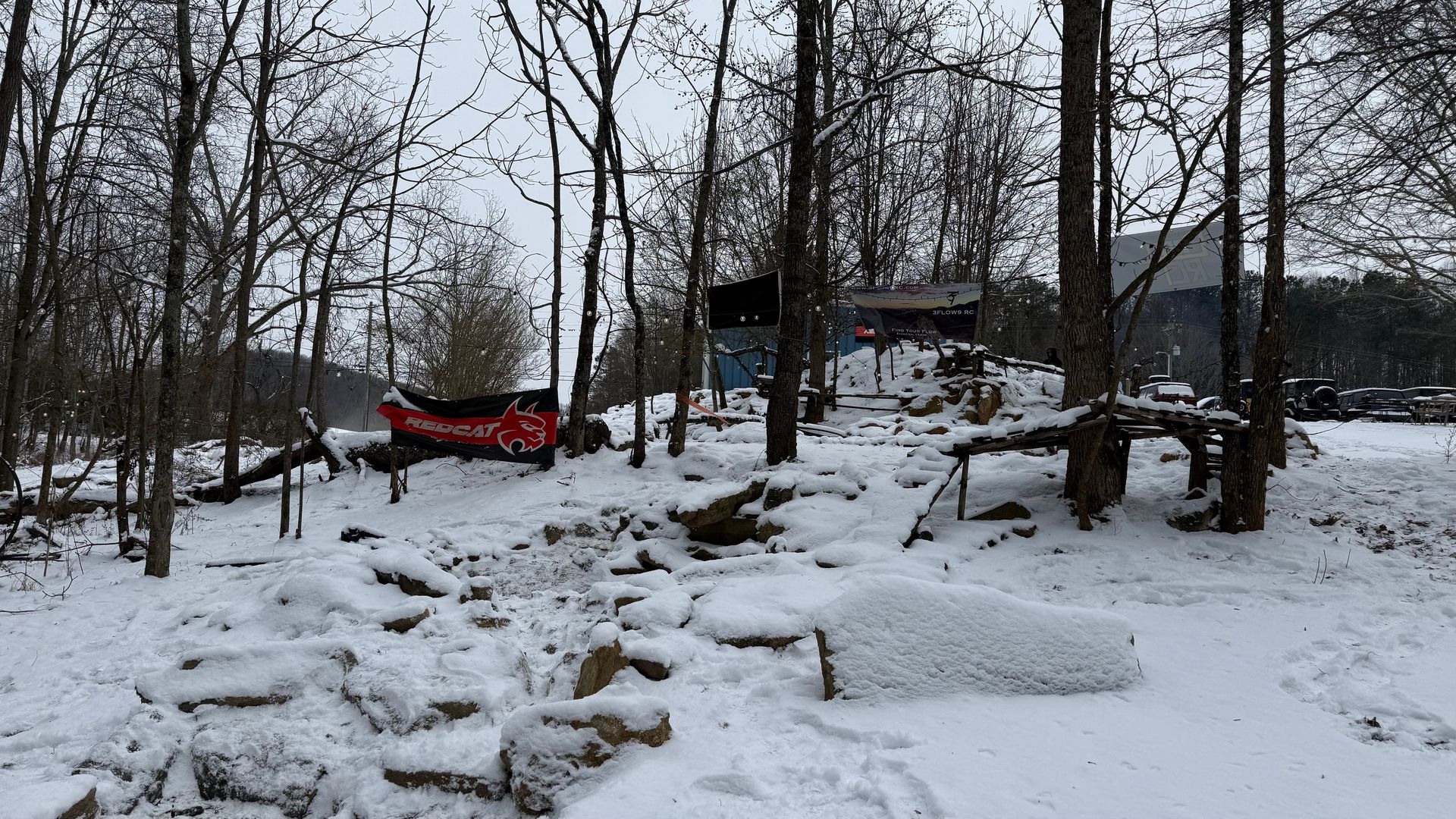 Snowy wooded yard with bare trees, a red canoe, rocks, and a house in the background.