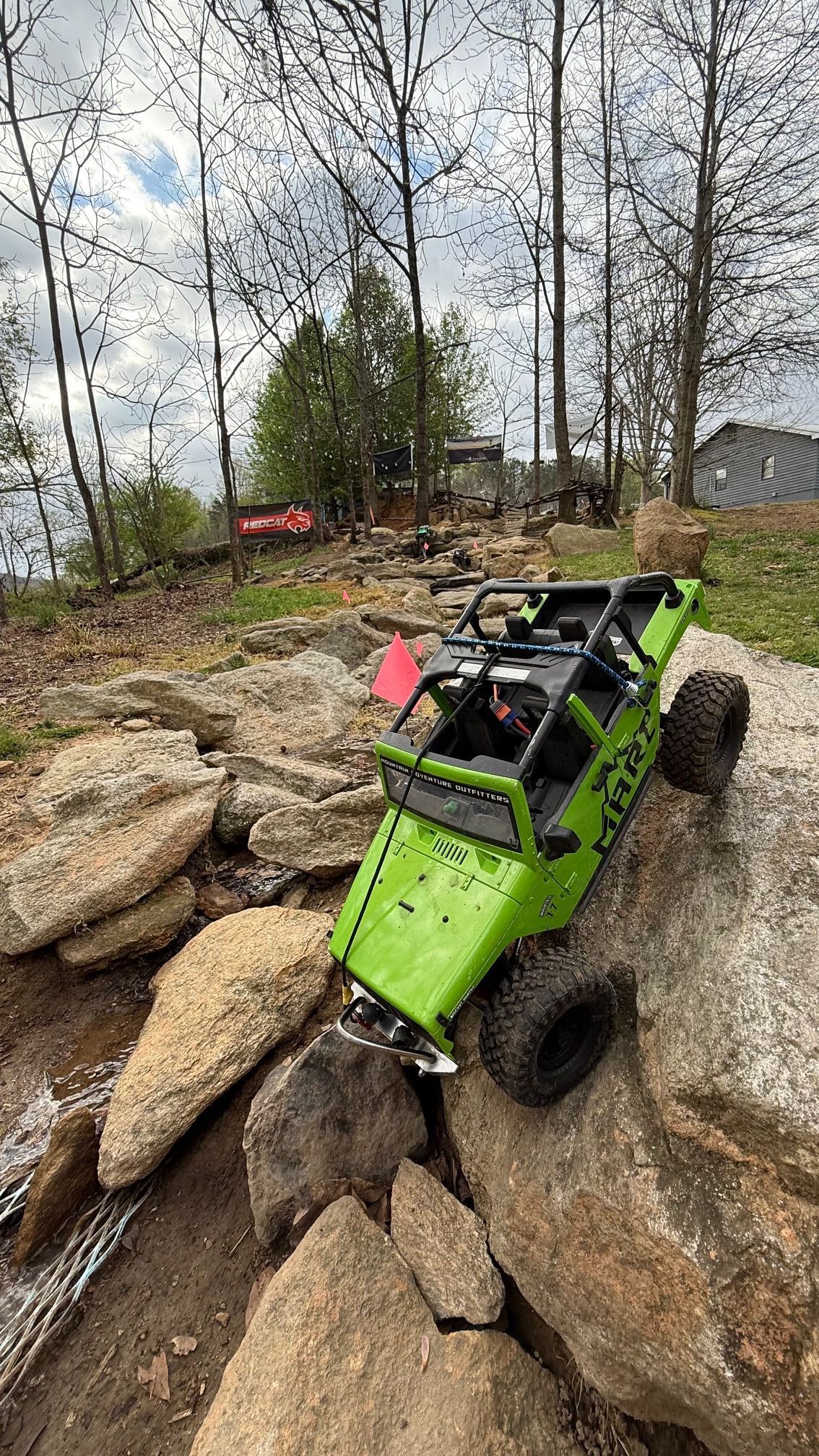 Green off-road buggy perched on large rocks in a wooded outdoor area