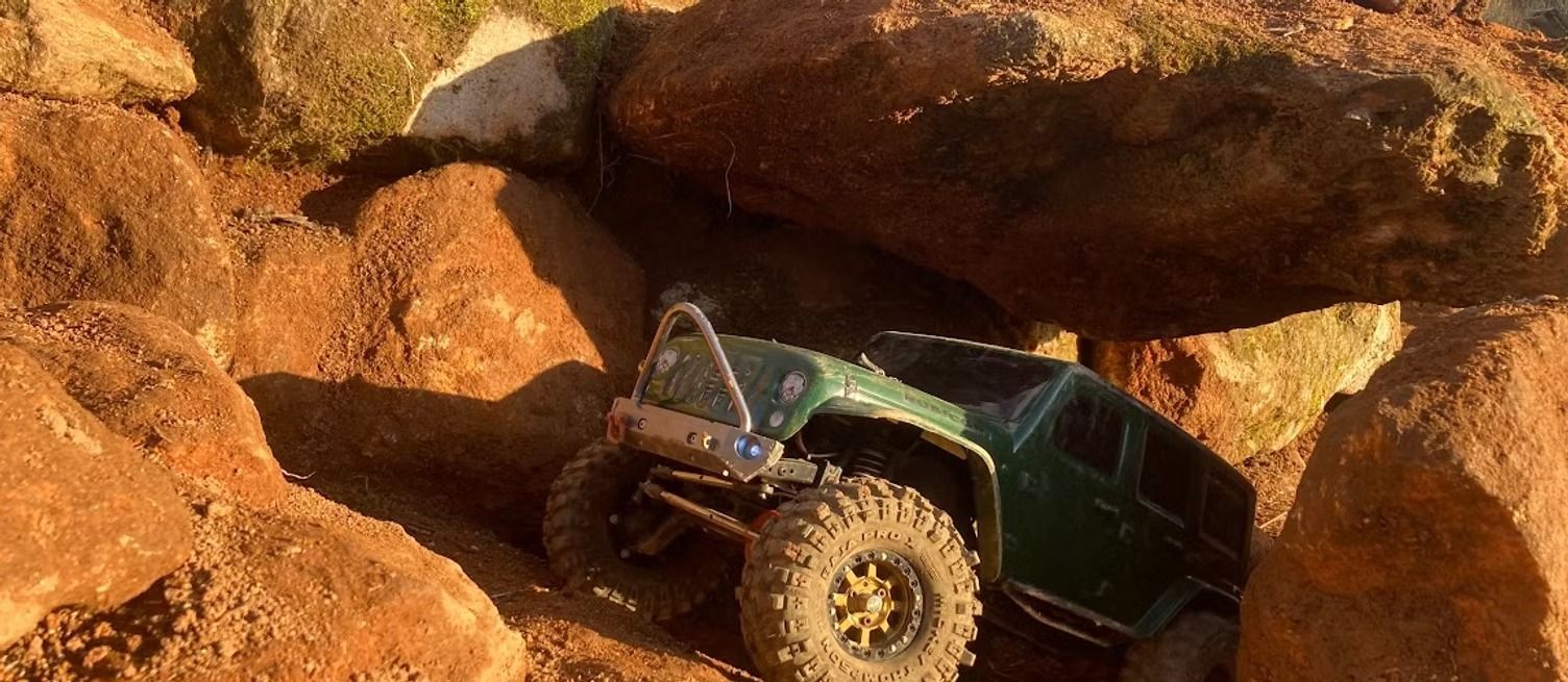 Off-road Jeep climbing over large red rocks in a desert landscape