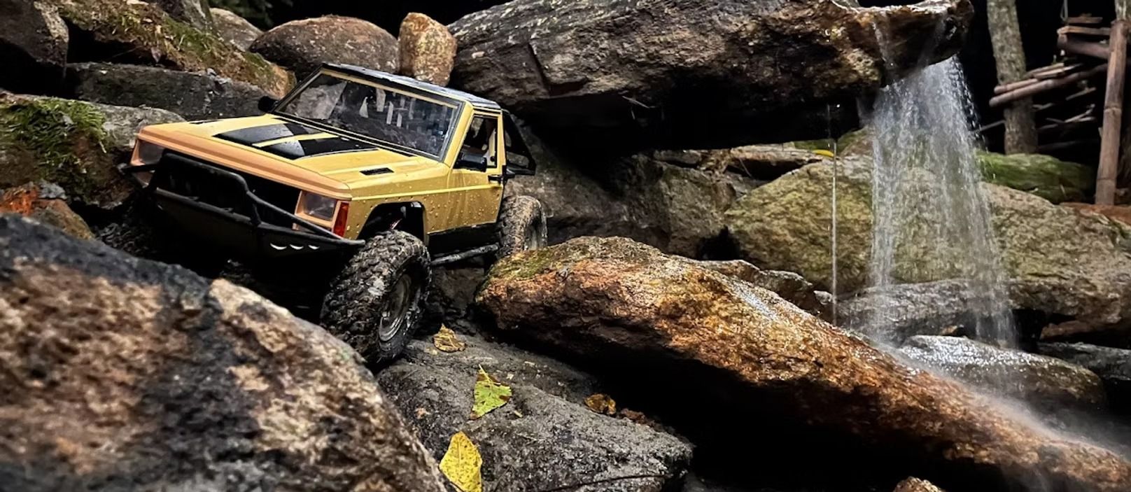 Yellow off-road truck climbing over wet rocks beside a waterfall