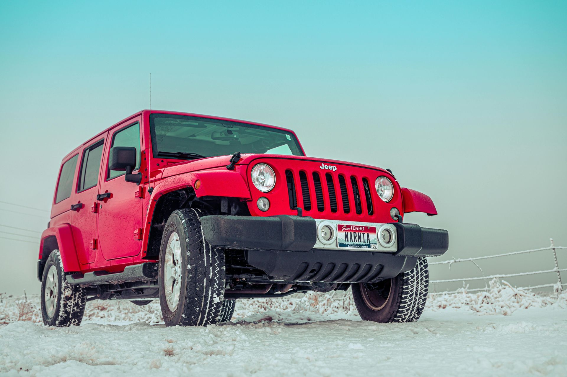 Red Jeep Wrangler parked in snow, against a pale blue sky.