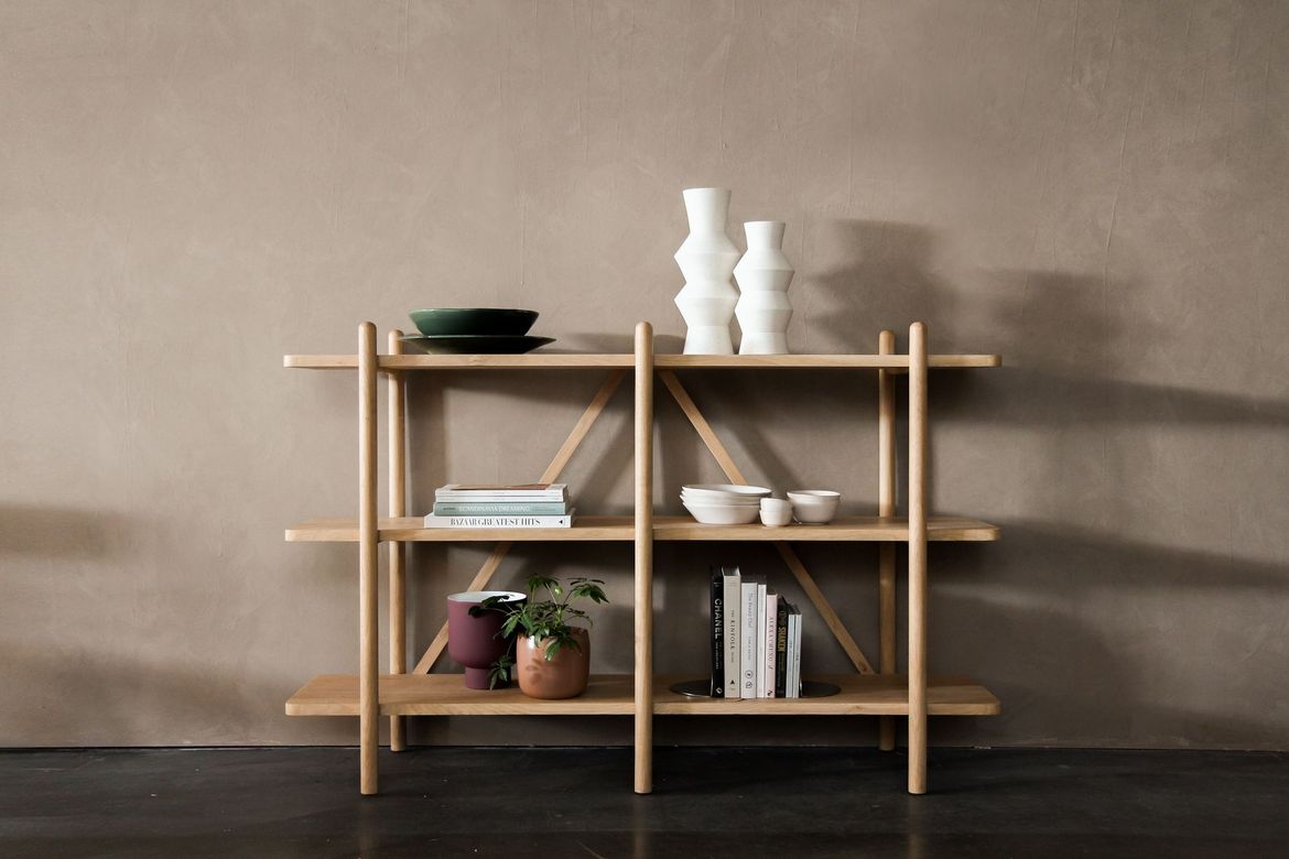 Scaffale minimalista in legno con libri, vasi, pianta e ciotole su una parete beige.