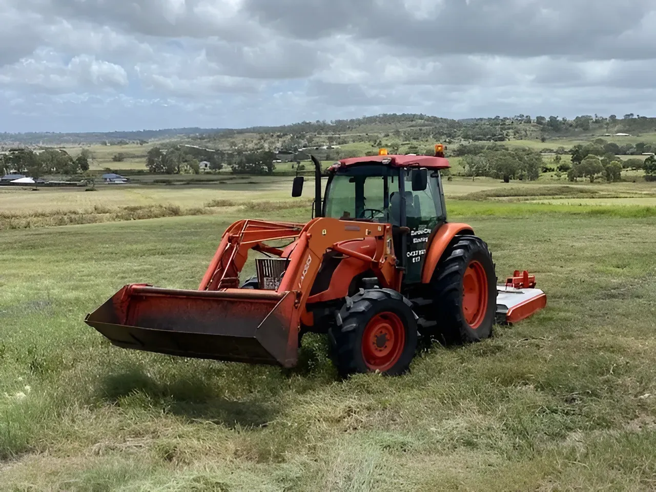 Orange Tractor With Front Loader on a Grassy Field Under a Cloudy Sky — Garden City Slashing in Highfields, QLD