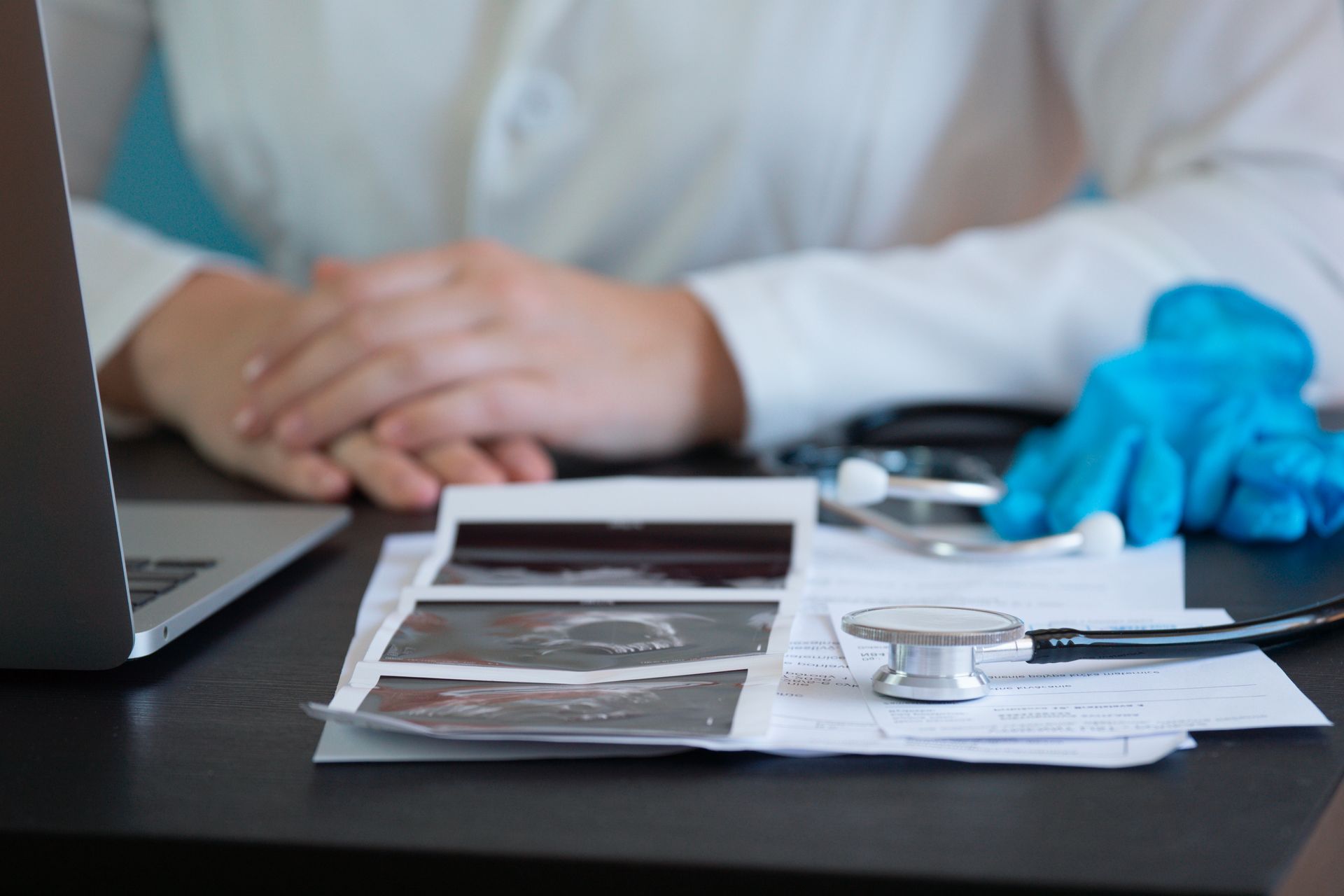 Medical consultation desk with ultrasound printouts, stethoscope, laptop, and blue gloves