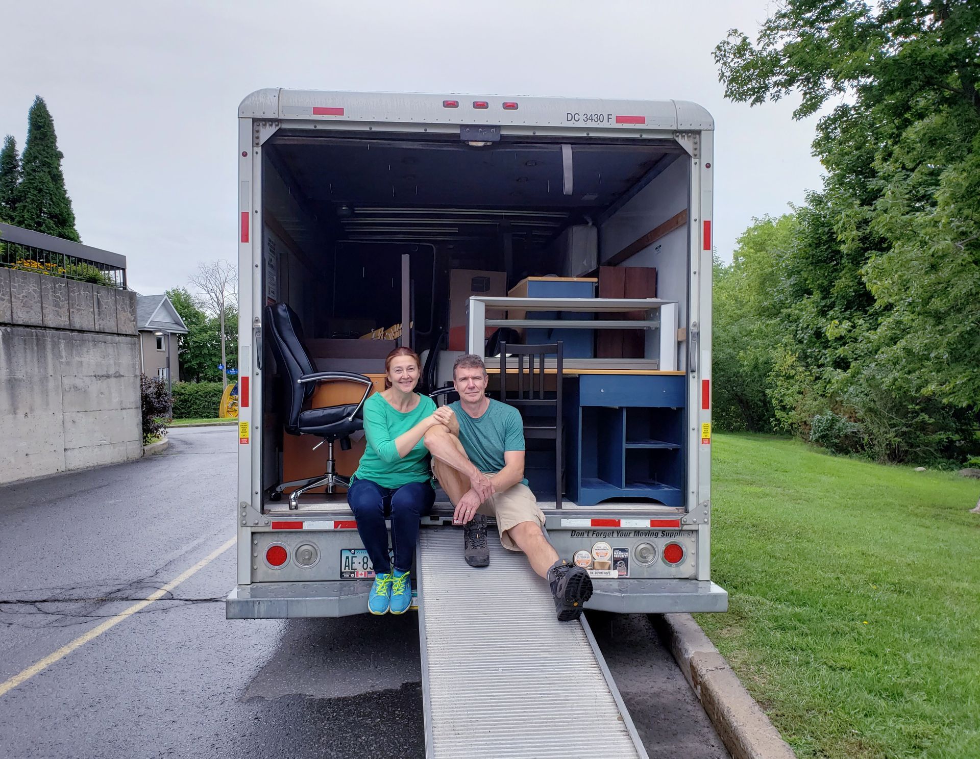 A man and a woman are sitting on the back of a moving truck.