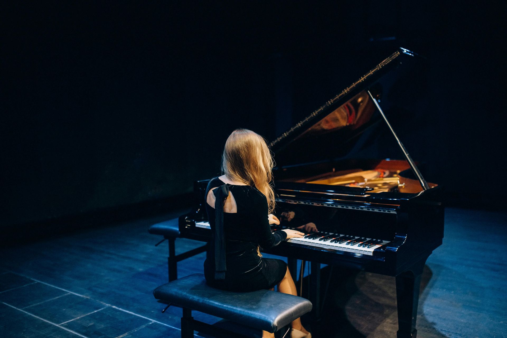 A woman is playing a grand piano in a dark room.