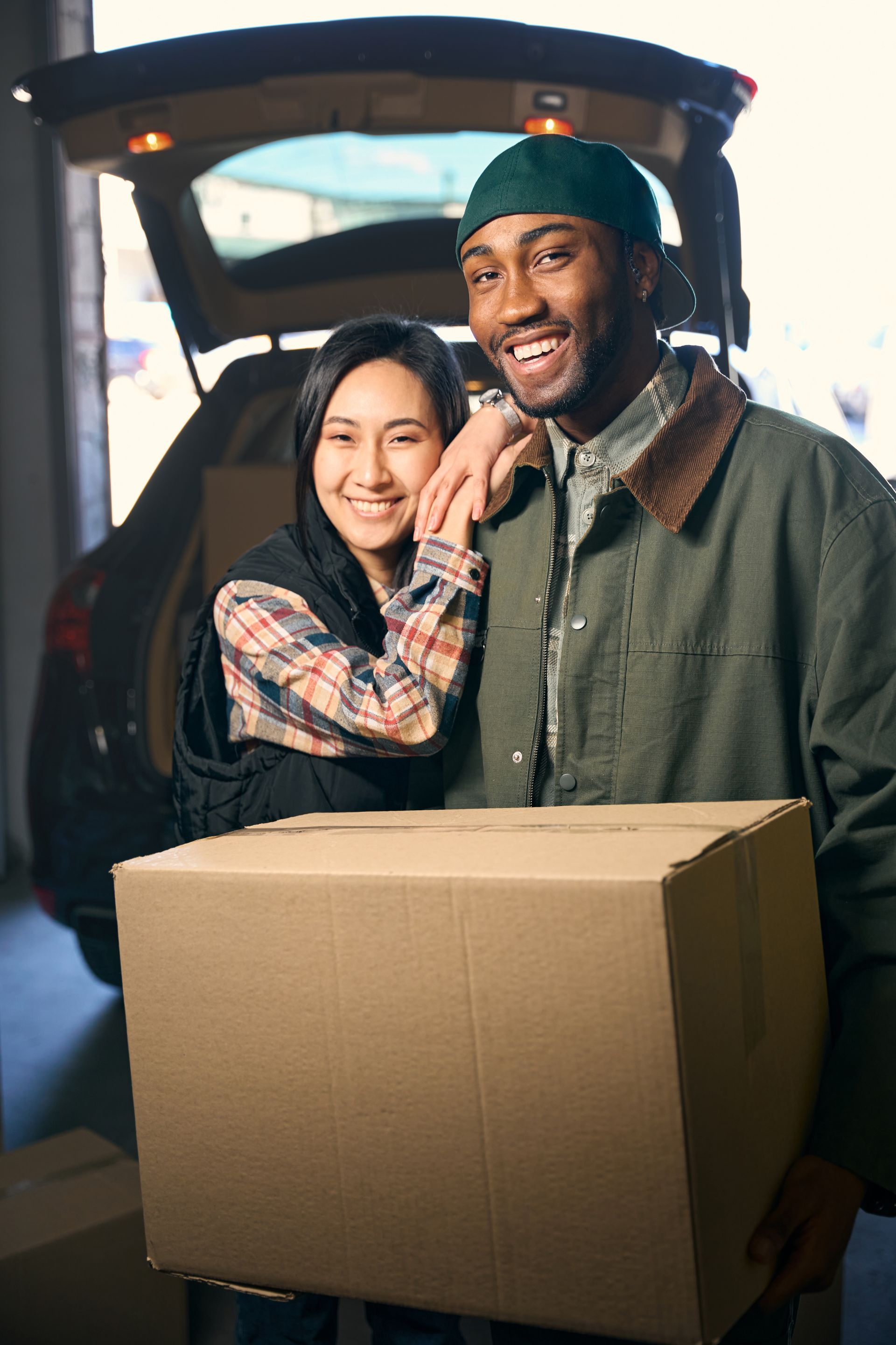 A man and a woman are holding a cardboard box in front of a car.