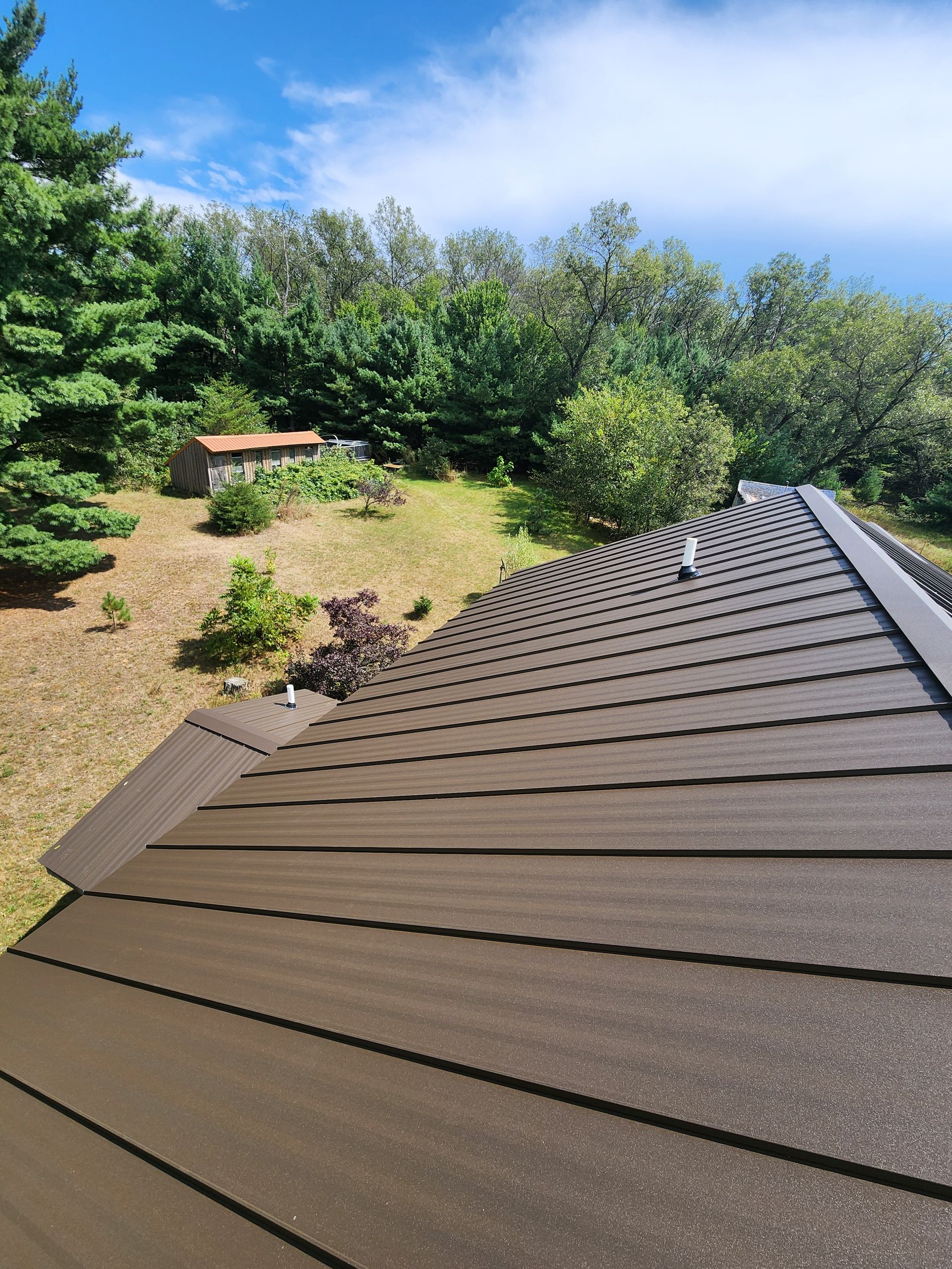 Brown roof tiles against a backdrop of green trees, grass, and a bright blue sky.