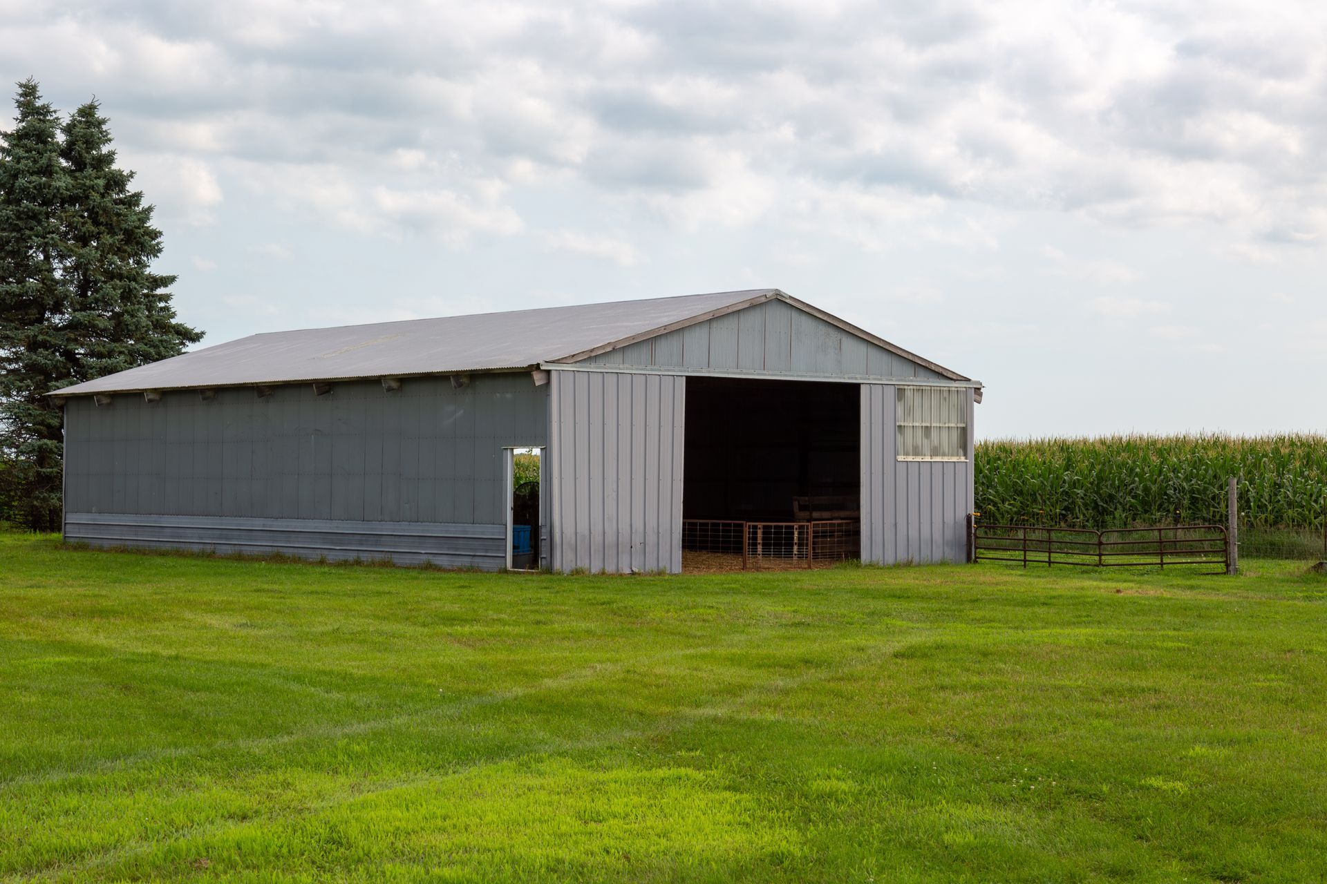 Large pole barn sitting in a grassy field beside a cornfield under a cloudy sky.