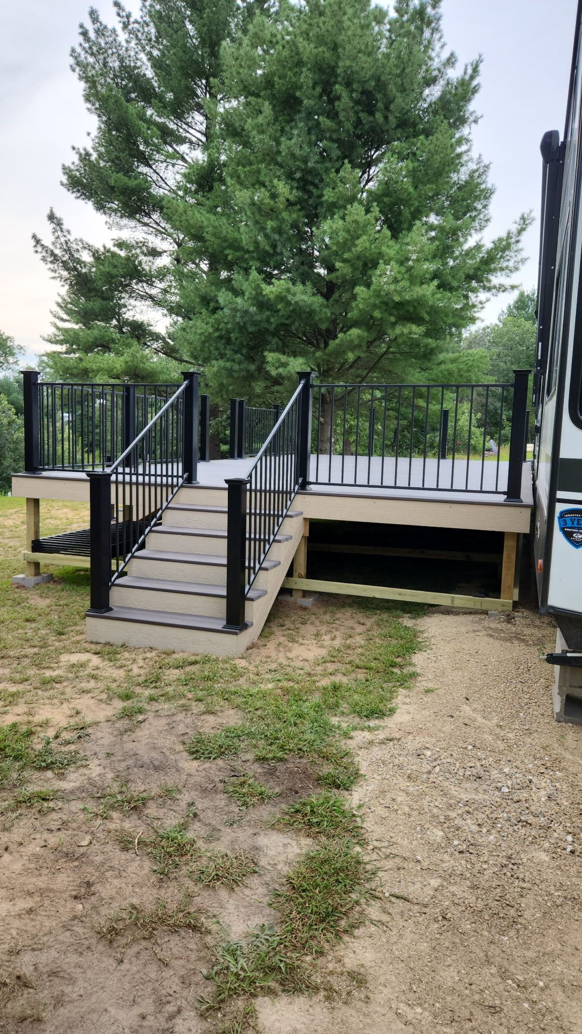 A wooden deck with black railings and steps leading to a green grassy area.