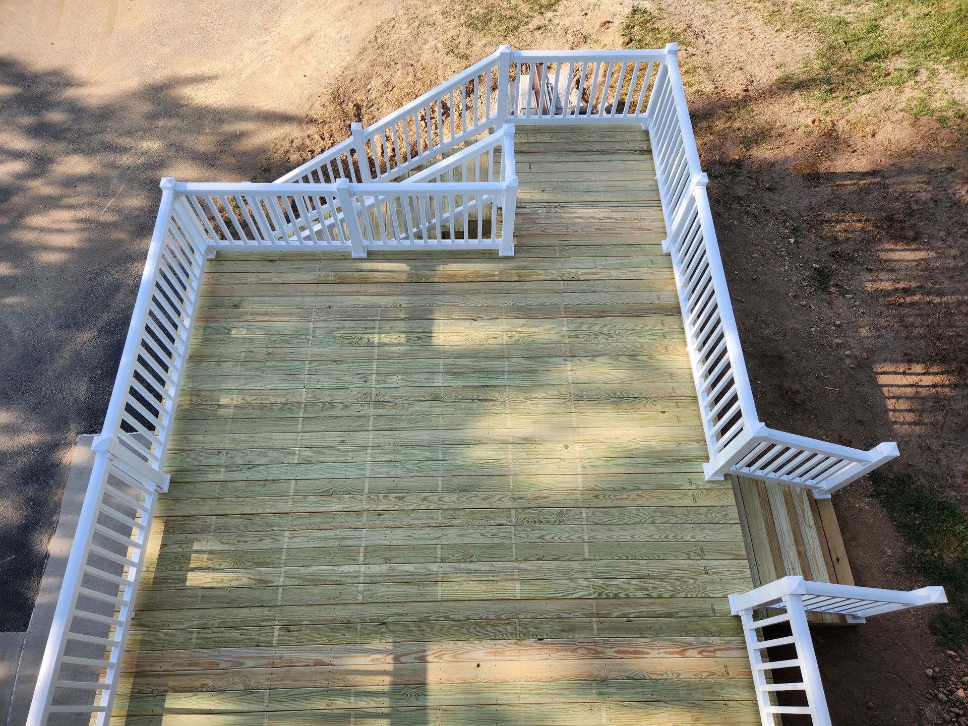 Overhead view of a wooden deck with white railings and steps outdoors.