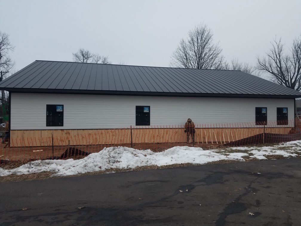 New construction building with light siding, dark roof and windows, and a person standing near it.