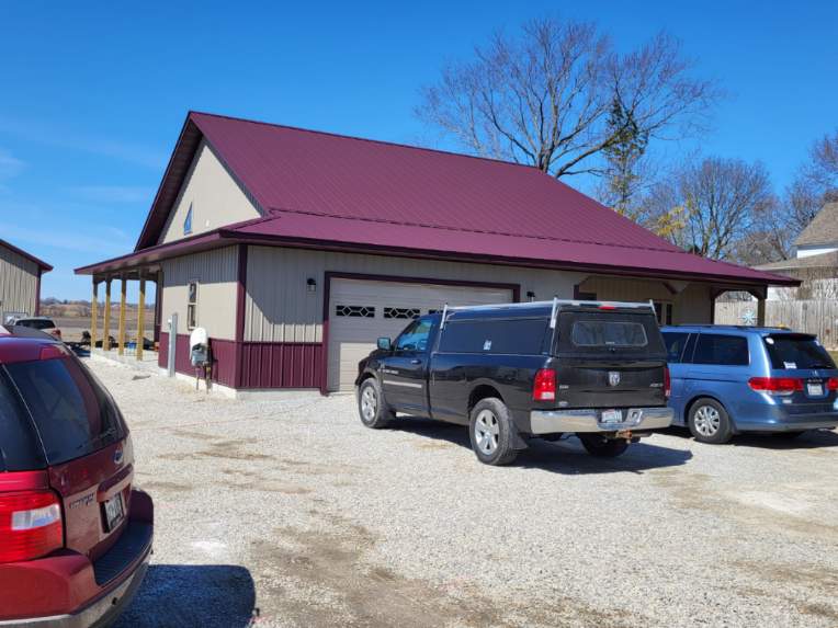 Tan building with burgundy roof and trim, three vehicles parked in gravel lot.