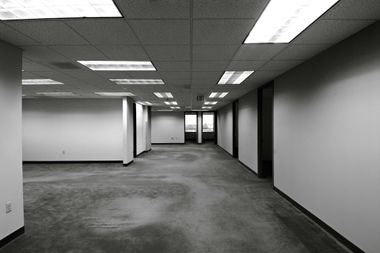 Empty office hallway with gray carpet, drop ceiling lights, and white walls.