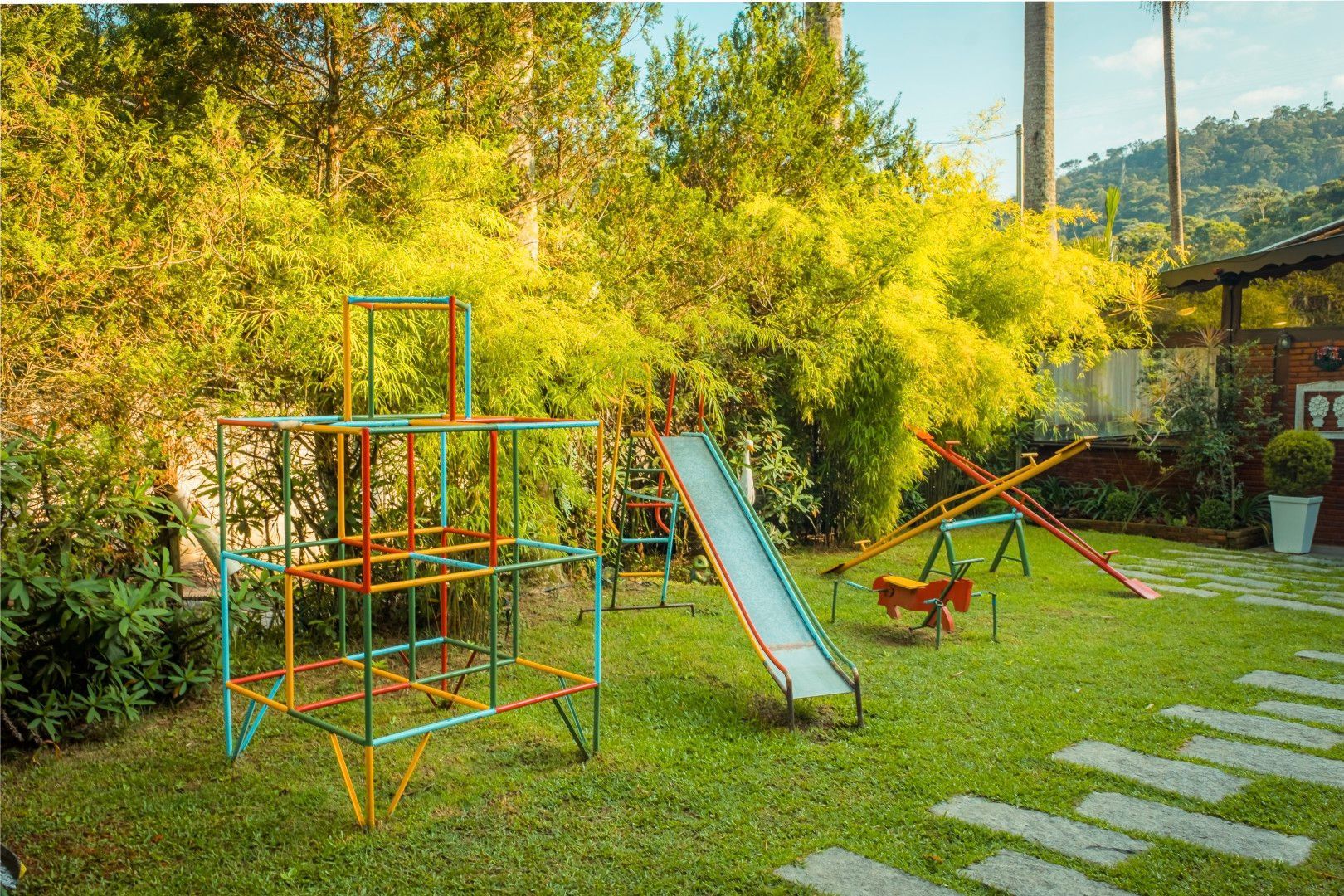 Parque infantil colorido no quintal com escorregador, estrutura de escalada e gangorra na grama.