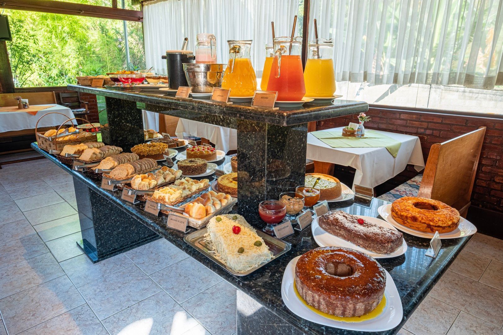Buffet de sobremesas em uma mesa preta com bolos, doces e suco de laranja em uma sala de jantar iluminada.