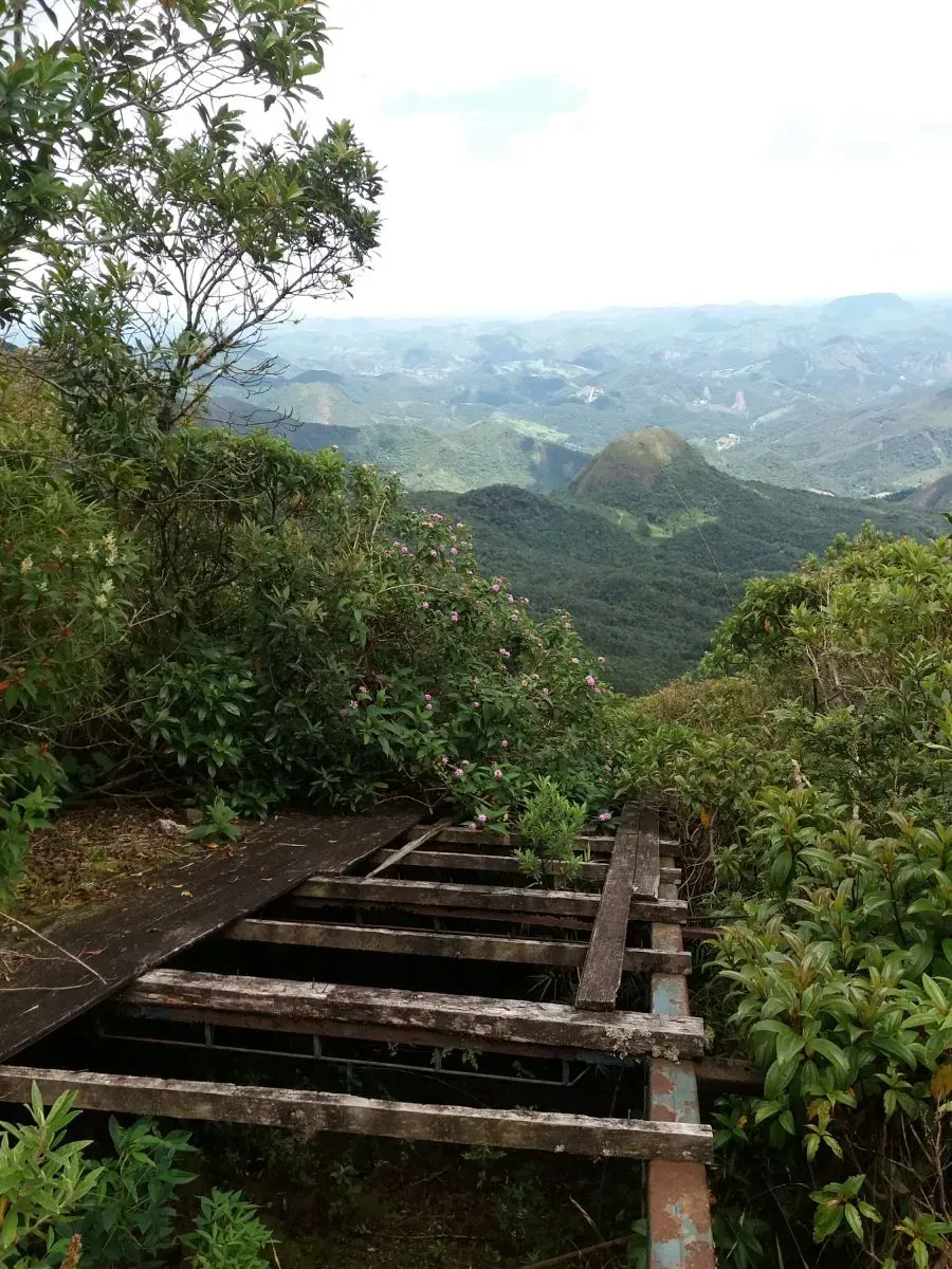 Mirante de madeira com vista para montanhas verdejantes envoltas em névoa e um vale arborizado.