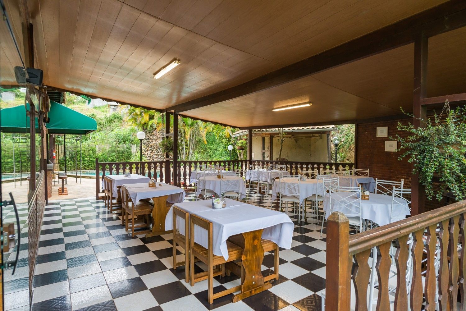 Pátio de restaurante ao ar livre com toalhas de mesa brancas, cadeiras de madeira e piso xadrez preto e branco.