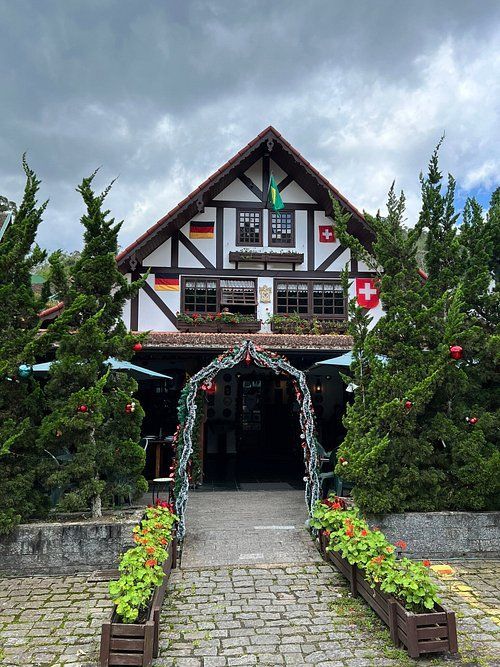Casa em estilo chalé com detalhes em madeira e caminho de pedra ladeado por flores sob um céu nublado.