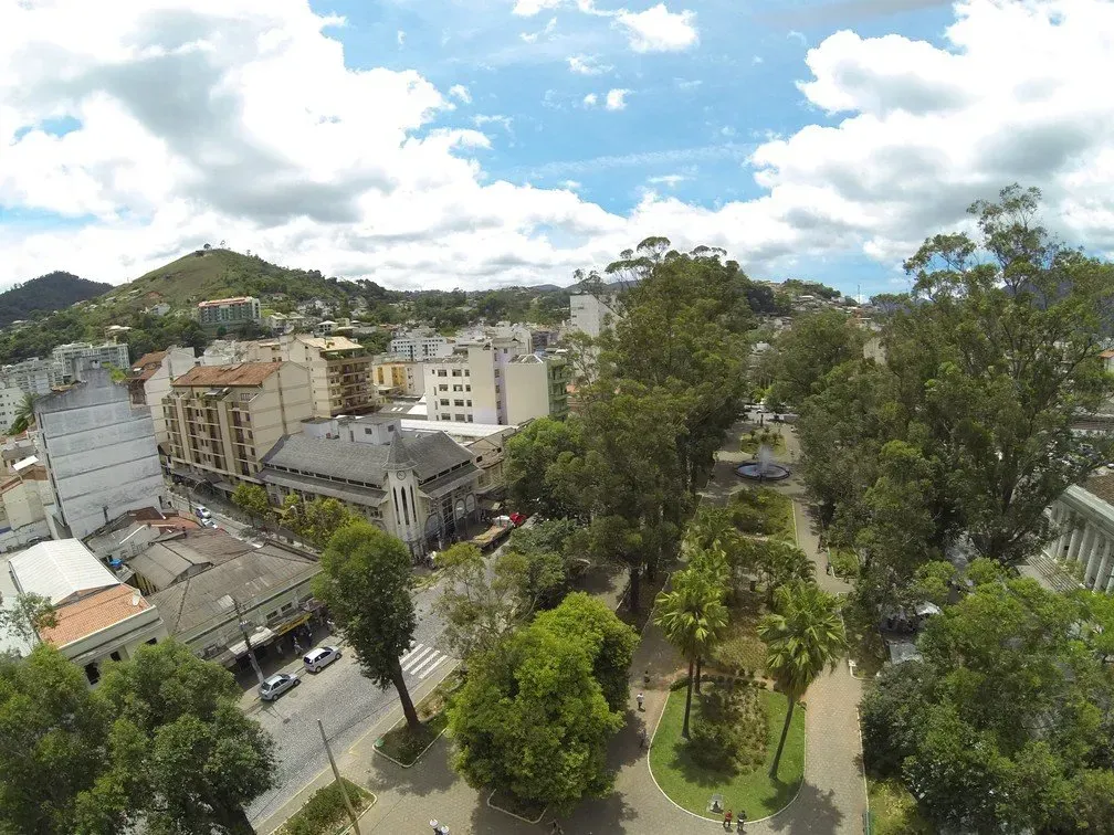 Paisagem urbana com árvores e edifícios sob um céu azul brilhante com nuvens dispersas.