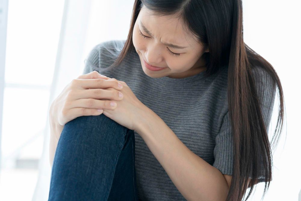 A woman is kneeling down and holding her knee in pain.