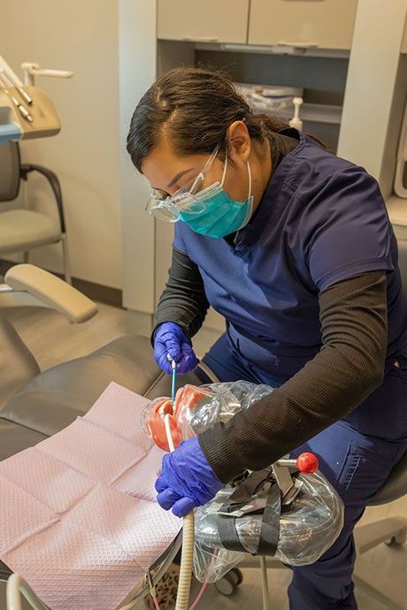 Dentist in blue scrubs and mask working on a patient in a dental chair with tools and gloves