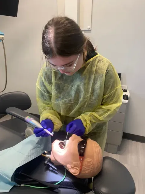 Dentist treating a patient in a dental chair, wearing protective gear and using a bright exam light.