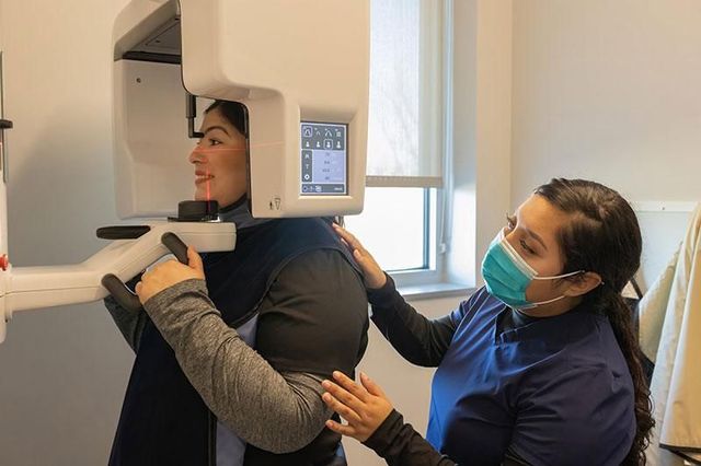 Dental technician adjusting an X-ray machine for a seated patient in a clinic