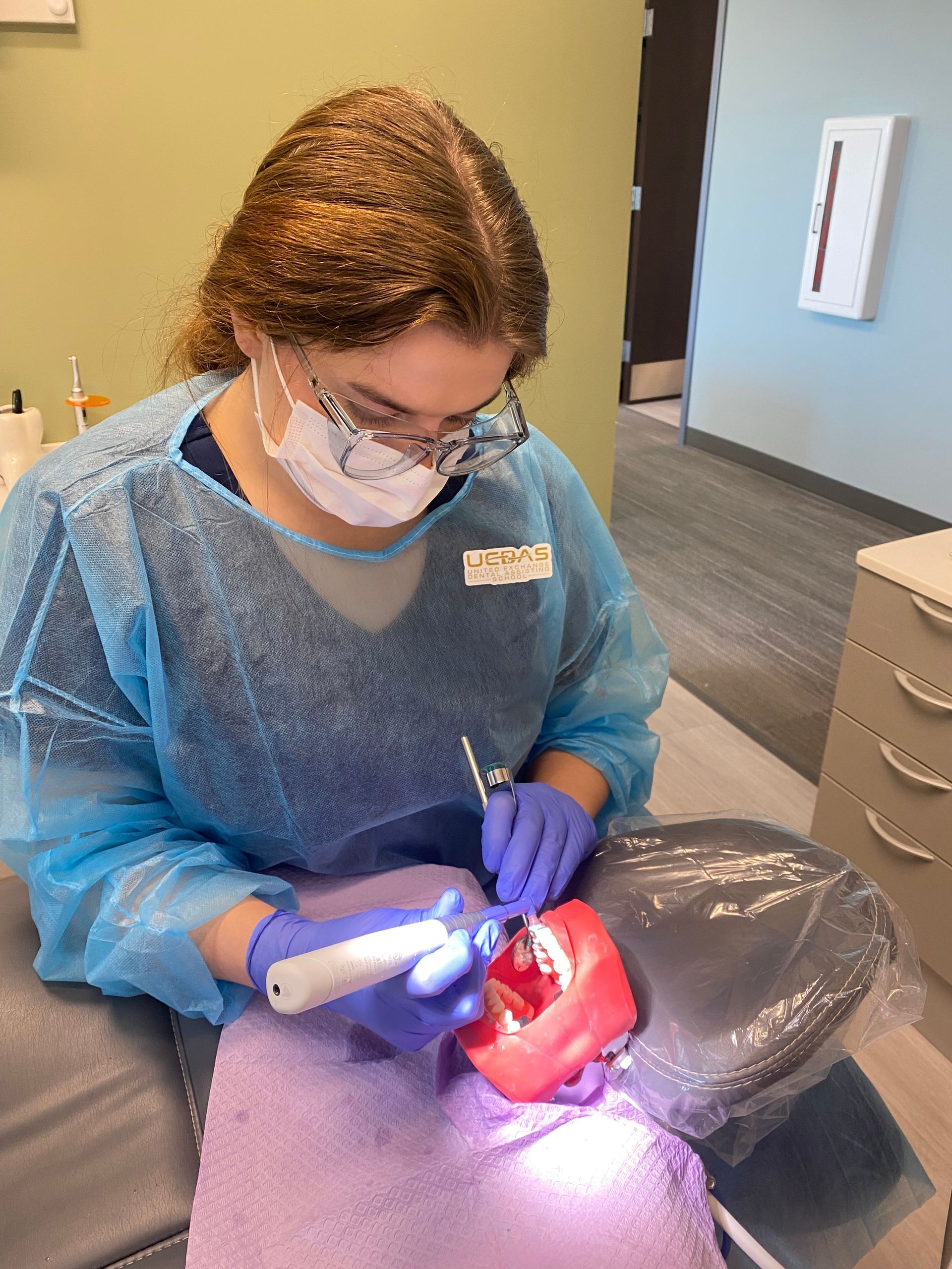 Dentist in blue PPE working on a patient with a bright mouth light in a clinic room