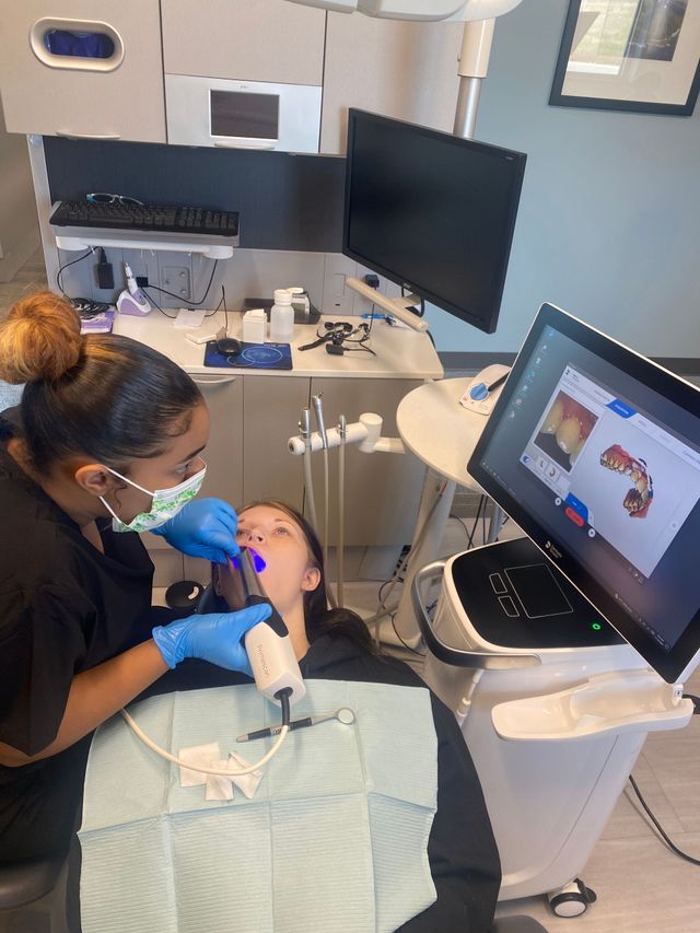 Dentist treating a child in a dental clinic, with a monitor showing a dental image.