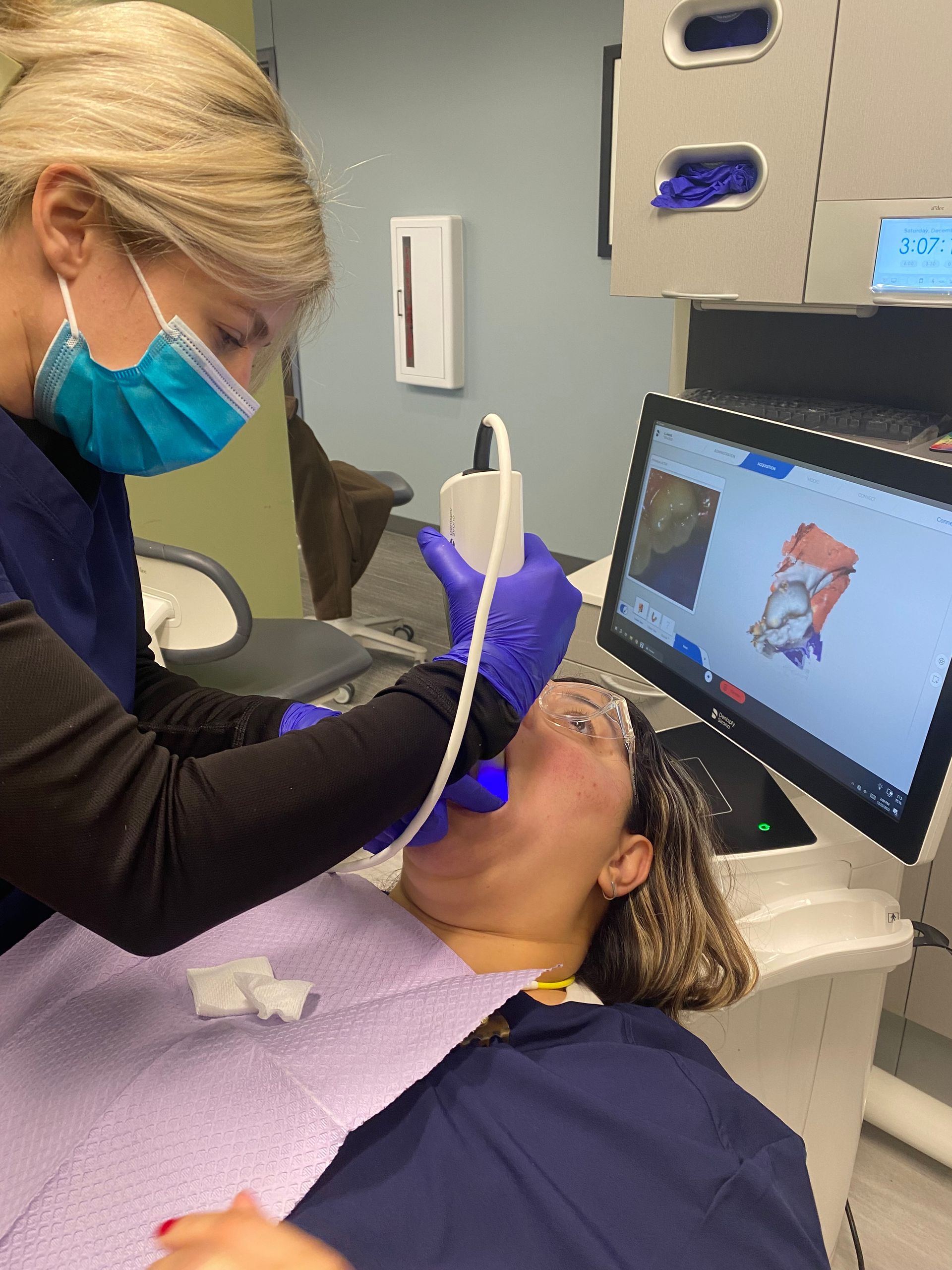 Dental hygienist using a scaler on a patient in a clinic, with monitor displaying a 3D dental scan.
